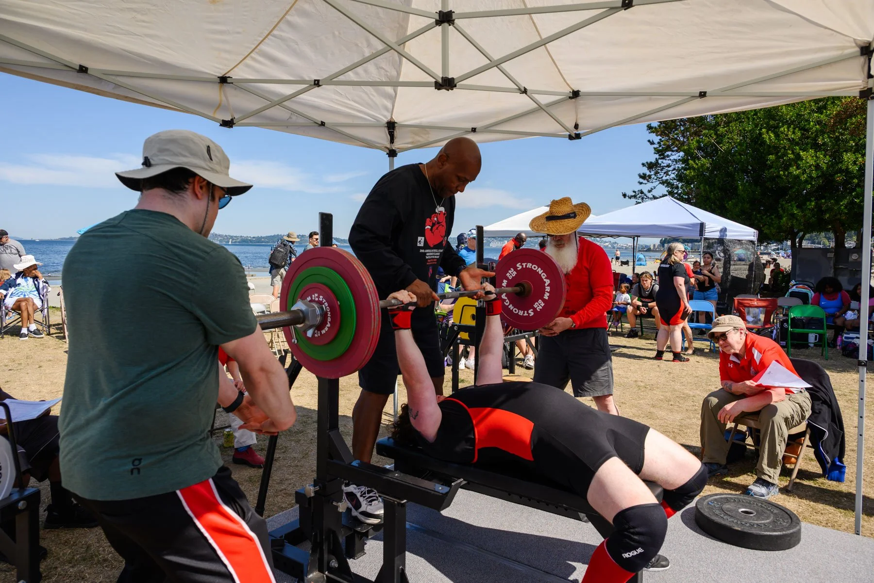 Bull Stewart and two other trainers spotting someone doing a chest press at Alki Beach powerlifting competition