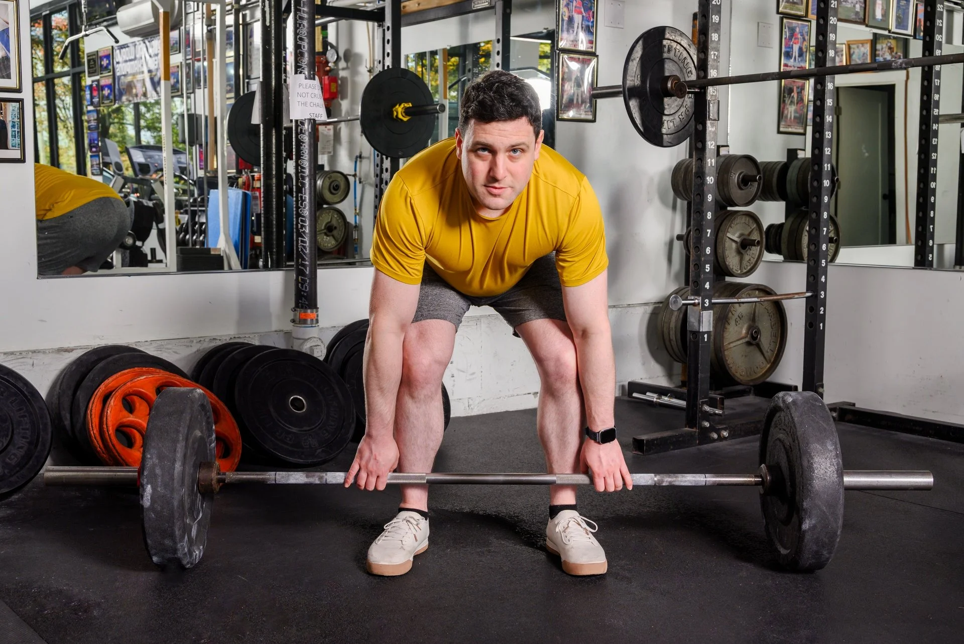 Man bending over about to lift heavy barbells and looking right into the camera