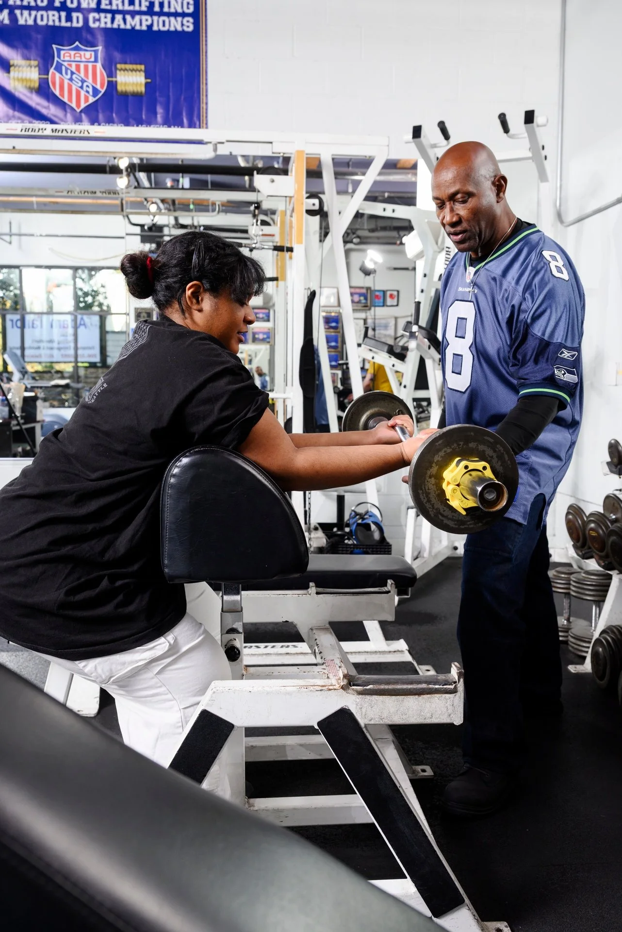 Bull Stewart coaching young woman who is doing bicep curls with small barbell