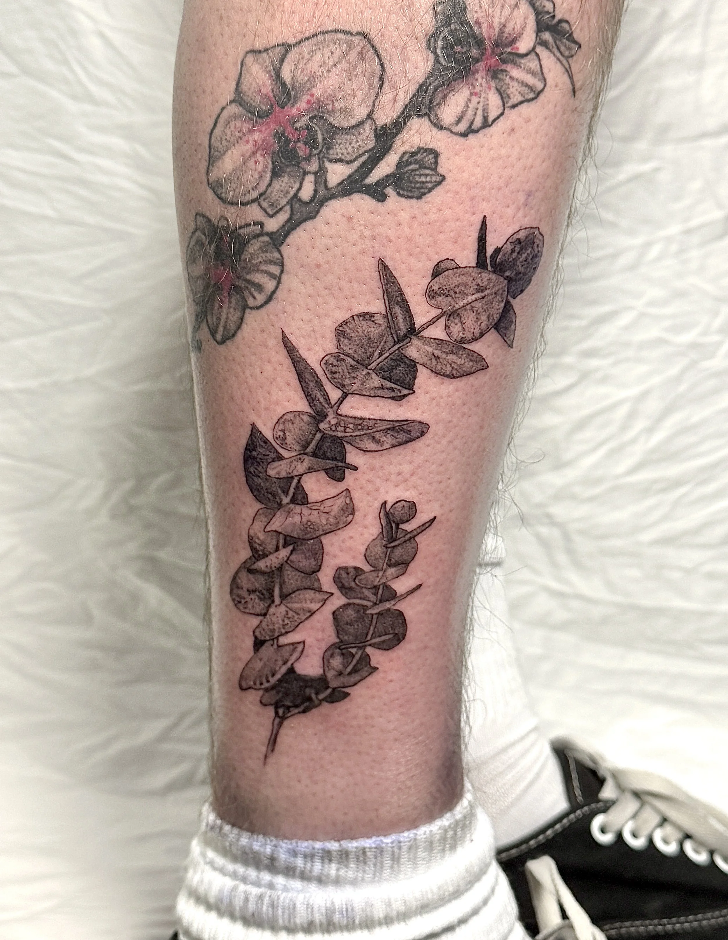 Black and gray tattoo of a branch with flowers and leaves on a person's forearm.