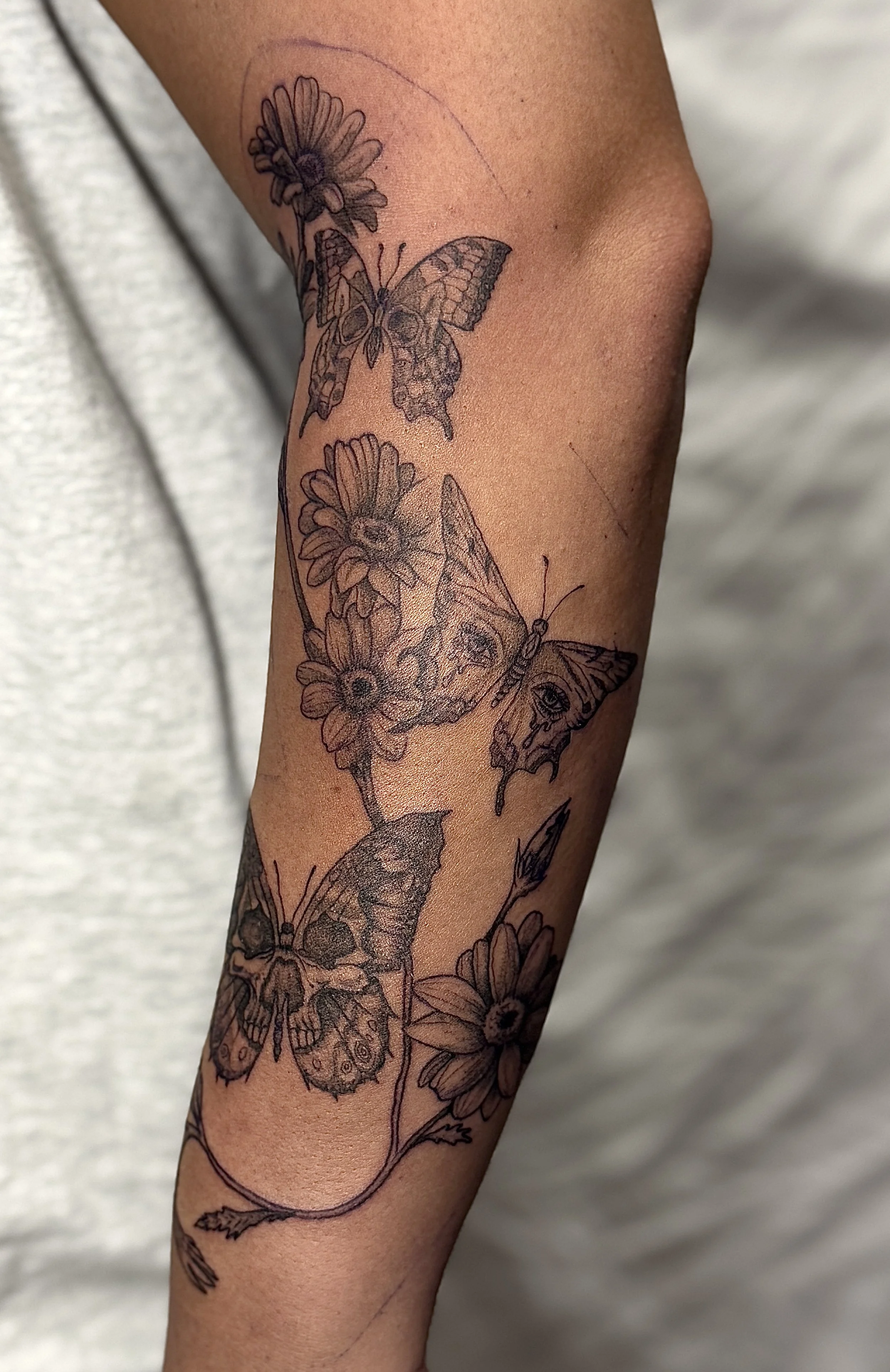 Black outline tattoo of butterflies and flowers on a person's forearm.