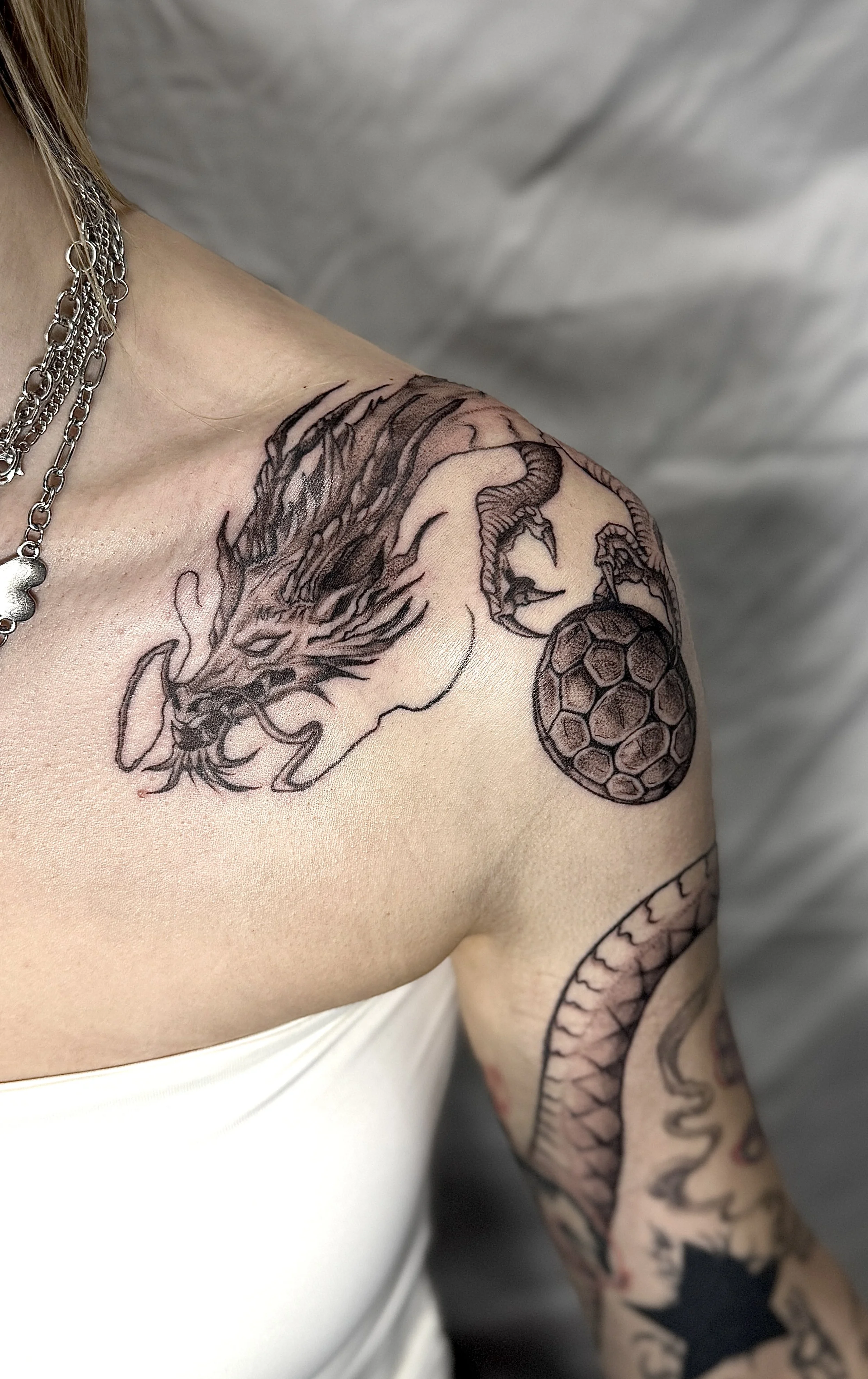Tattoo of a dragon on the person's shoulder with a snake wrapped around a sphere on the arm.