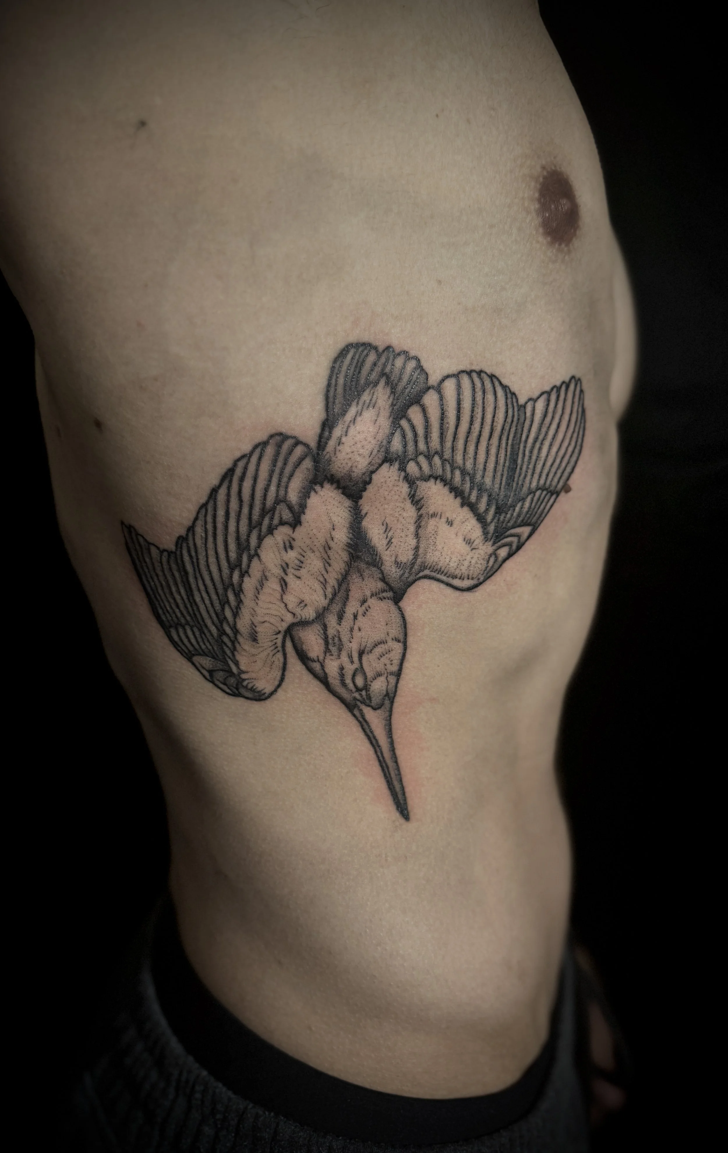 A black and white tattoo of a bee with detailed wings and body, perched on a large flower, on a person's side ribcage.