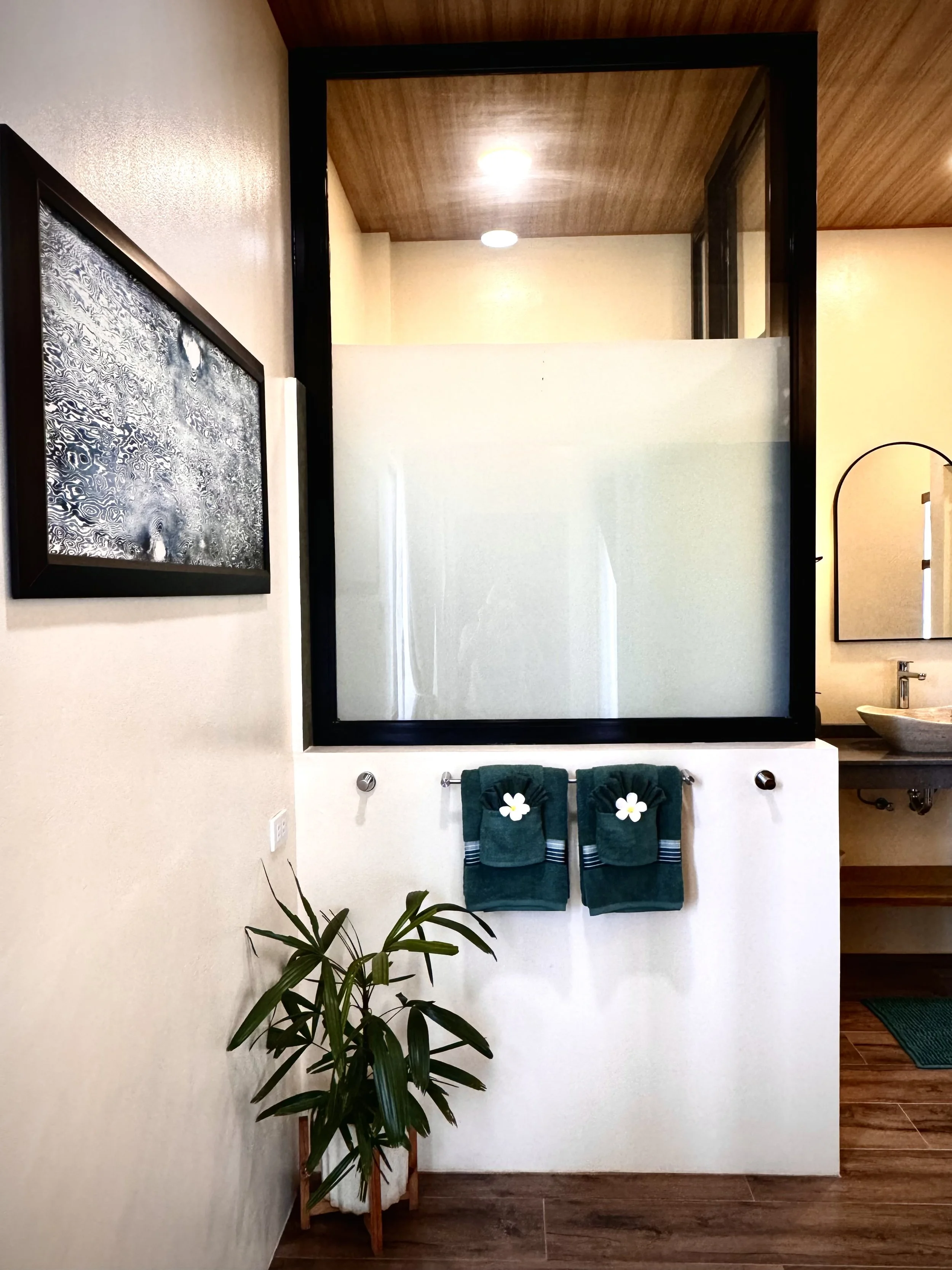 Bathroom with two green towels hanging on a towel rack, a potted plant on a wooden stand, and a mirror on the wall.