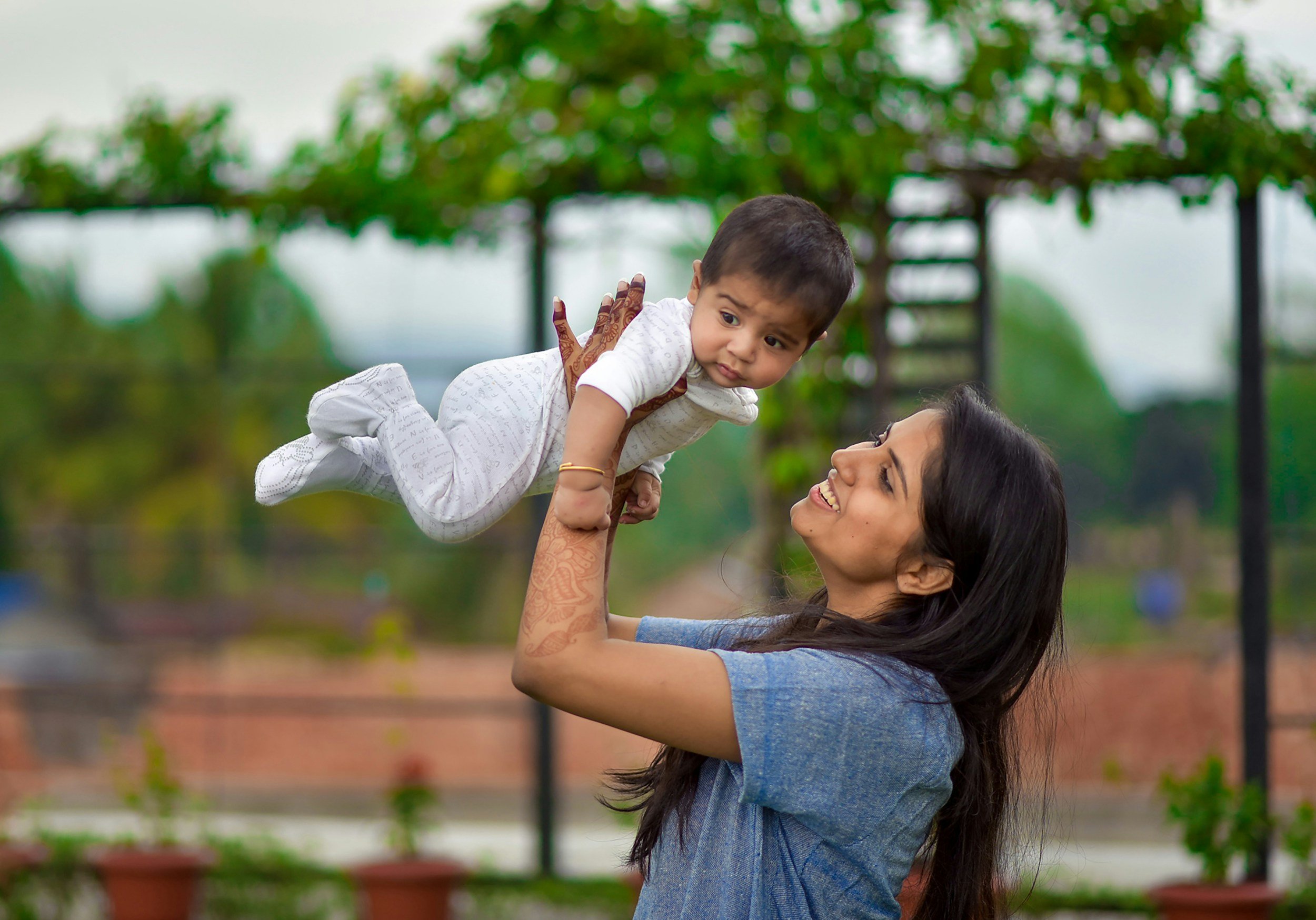 Mother smiling as she lifts her baby outdoors, representing family wellbeing and chiropractic care supporting pregnancy, birth and early childhood development.