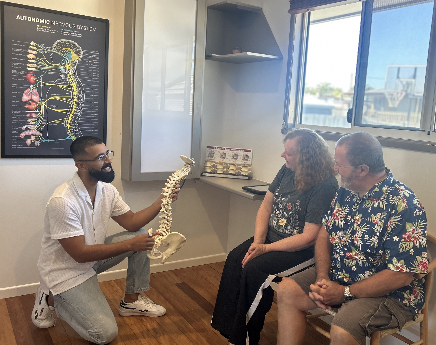 Chiropractor at Vibrant Family Chiropractic using a spine model to explain spinal health and chiropractic care to two patients during a consultation.