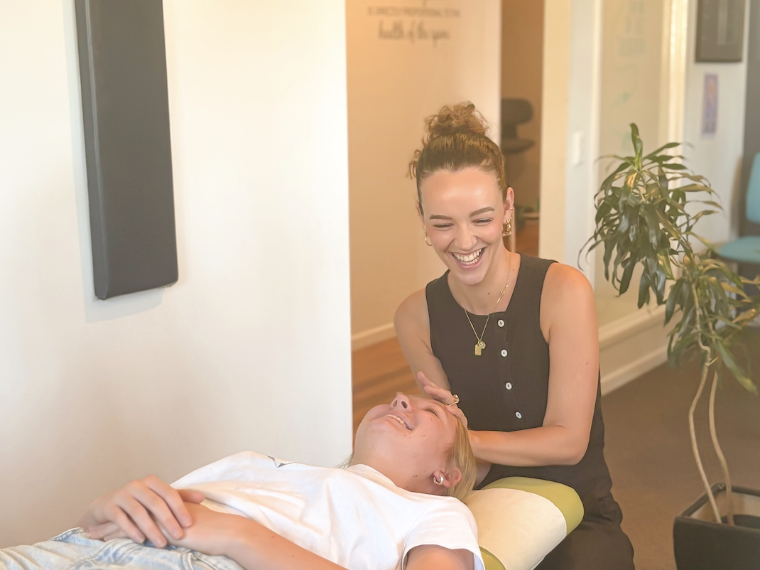 Smiling practitioner performing a neck examination on a reclining woman in a wellness clinic