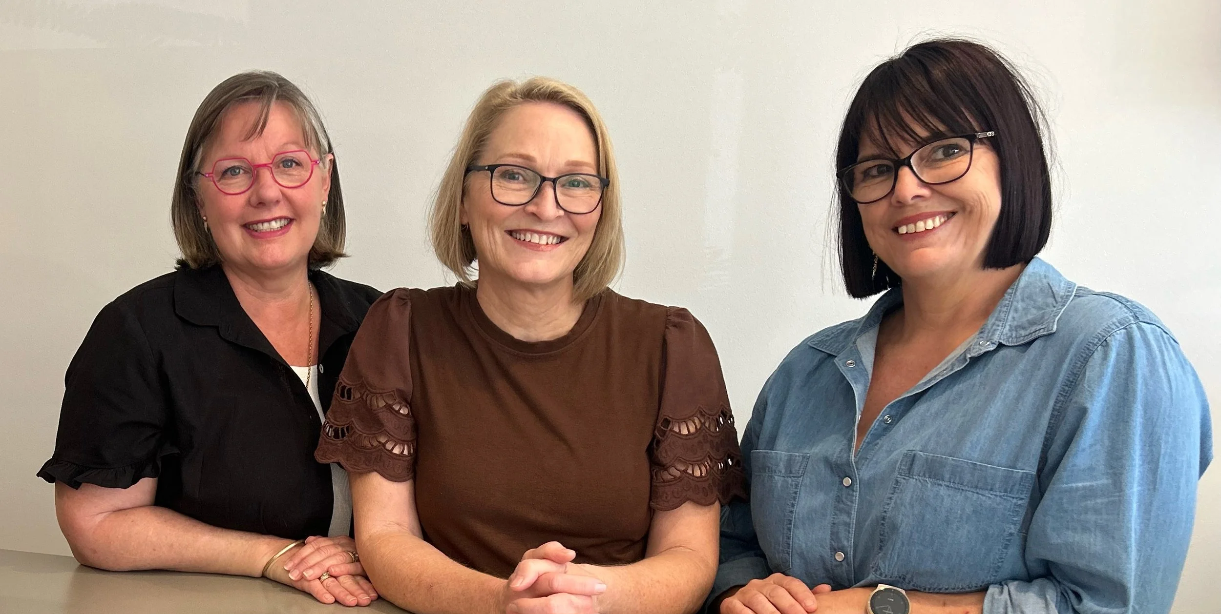 The friendly Vibrant Family Chiropractic assistants team smiling together at the clinic reception desk.