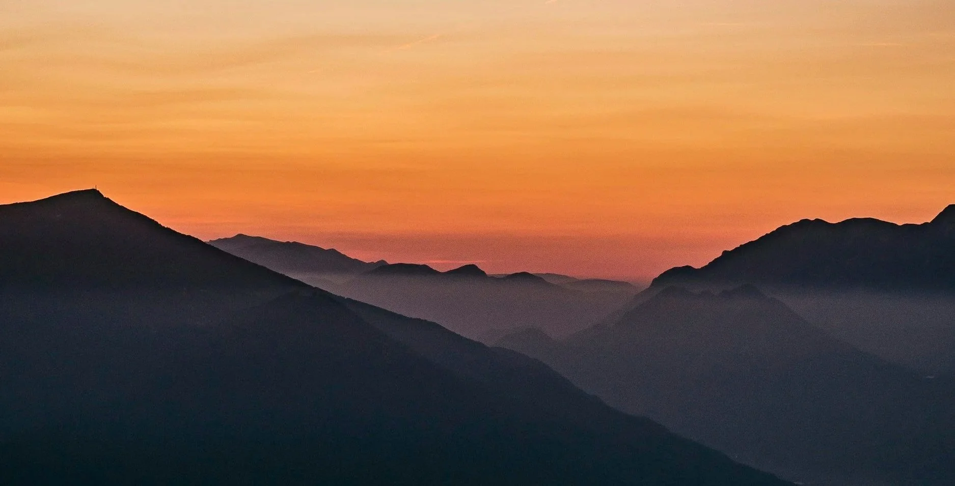 Layered mountain silhouettes beneath a glowing orange sunset sky