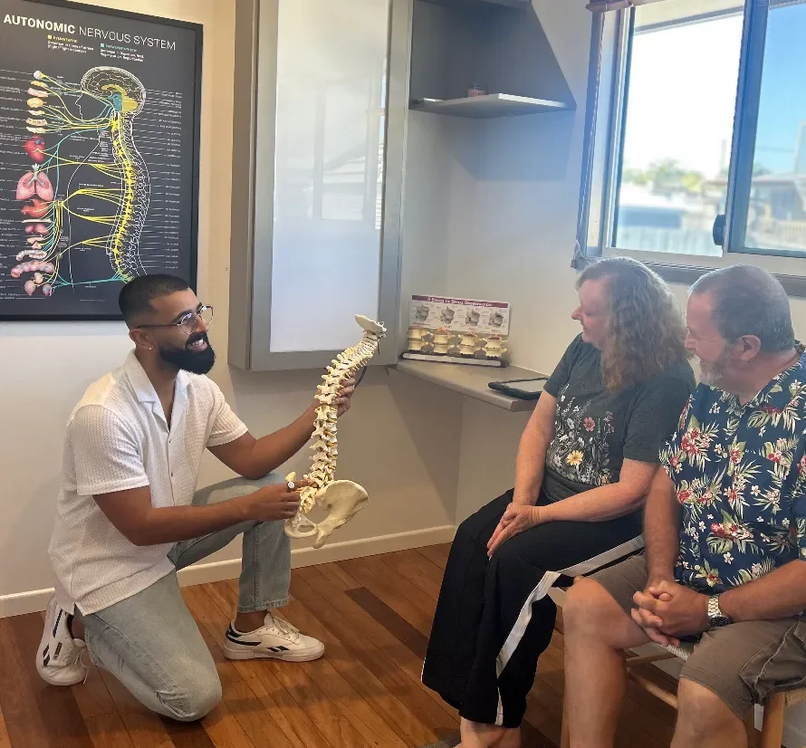 Chiropractor at Vibrant Family Chiropractic using a spine model to explain spinal health and chiropractic care to two patients during a consultation.