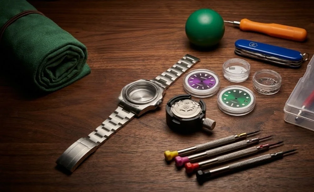 Various watch repair tools and parts on a wooden surface, including a green exercise ball, small screwdrivers, watch faces, a partially disassembled watch, a Swiss Army knife, a green towel, and a small container with watch parts.