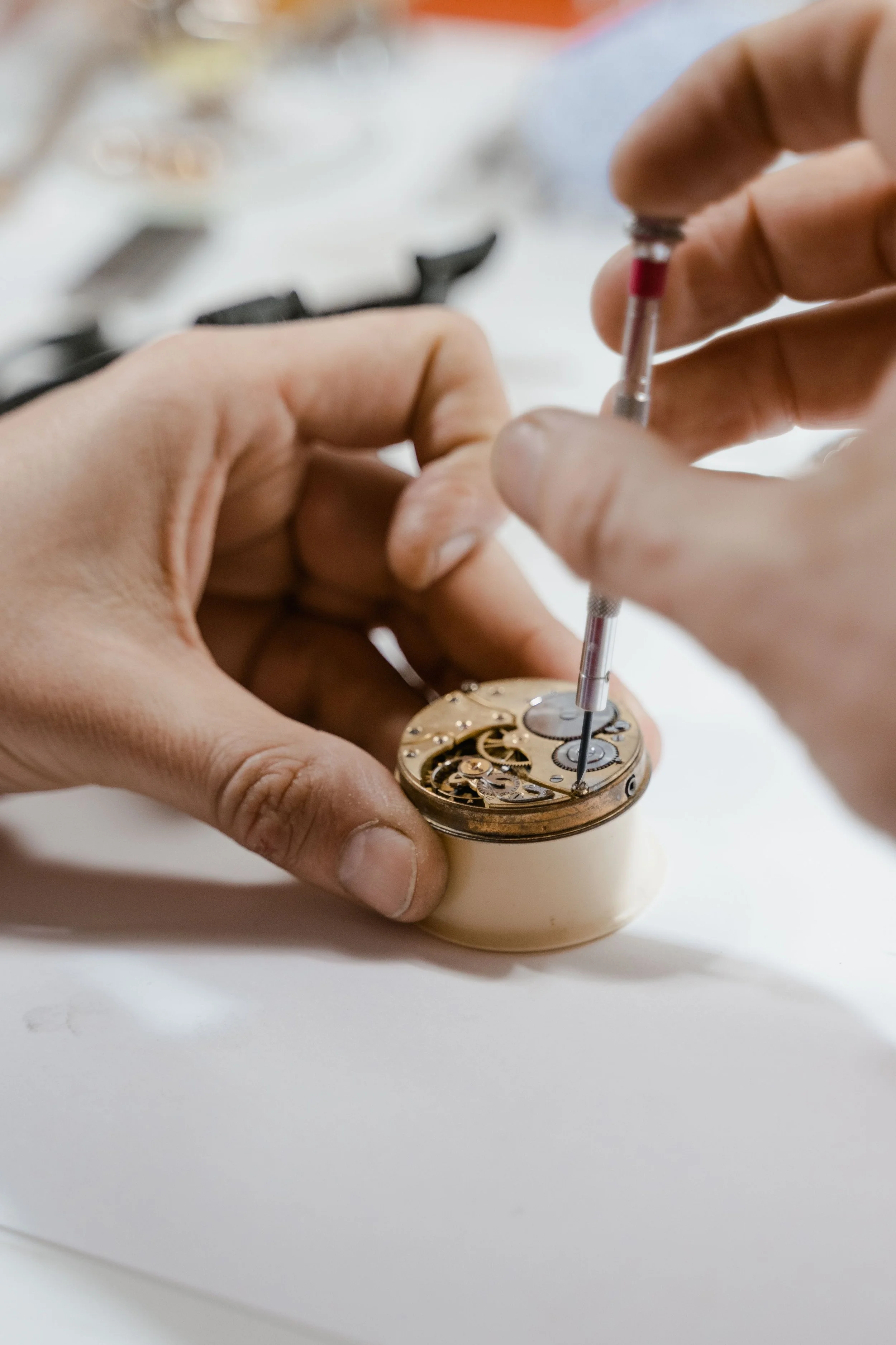 Close-up of hands working on the inner mechanism of a watch, with small gears and tools visible.