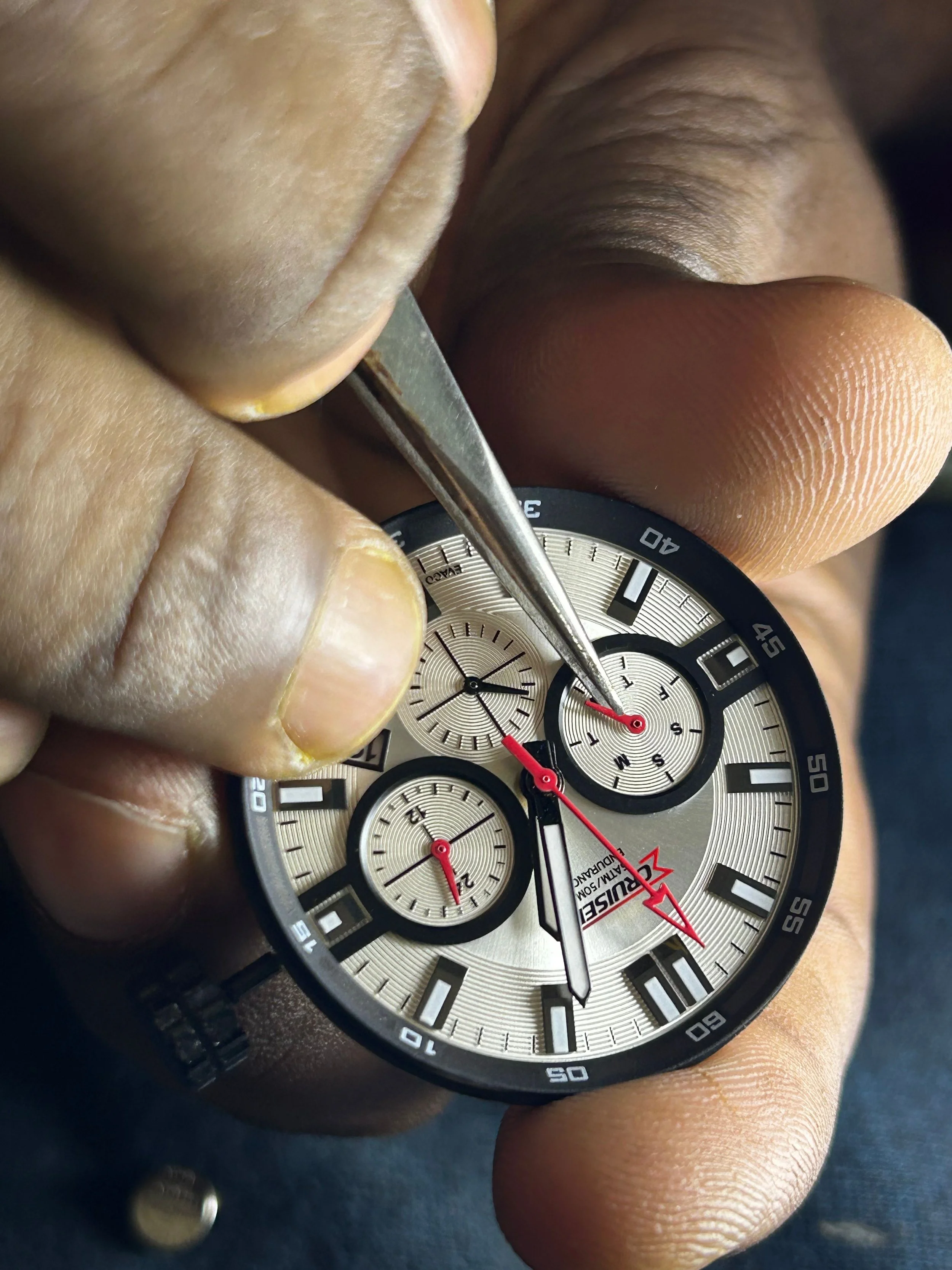 A person is adjusting the knobs of a silver-colored wristwatch with a black strap and multiple subdials.