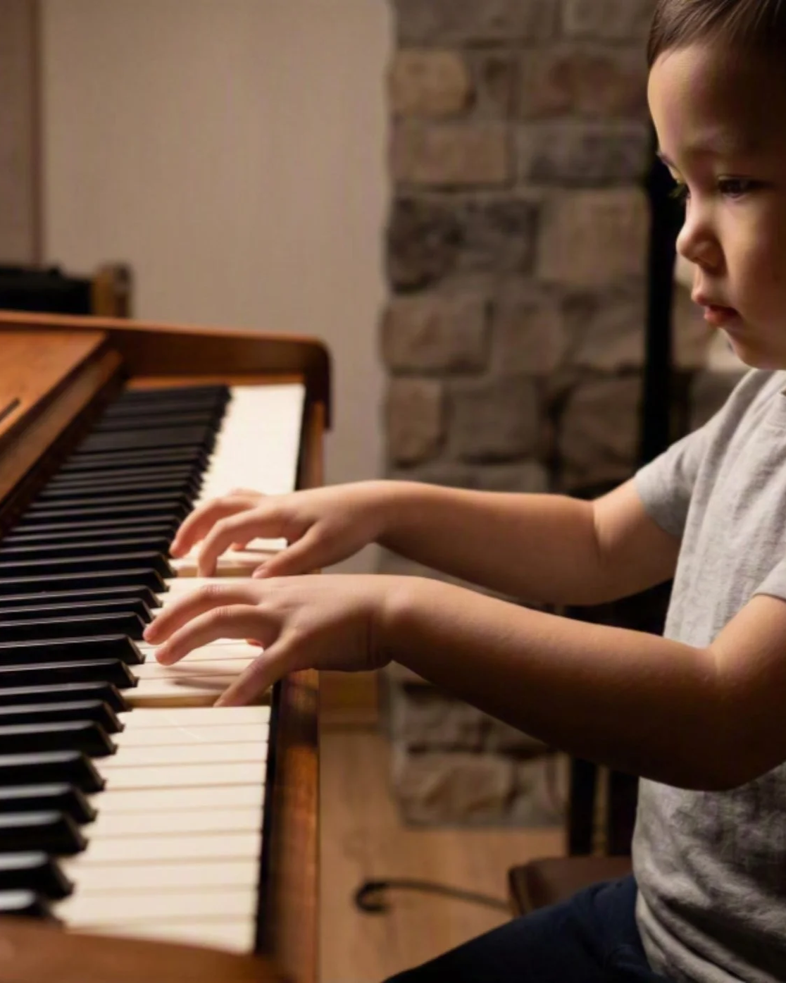 A young boy playing a piano with a brick wall in the background.