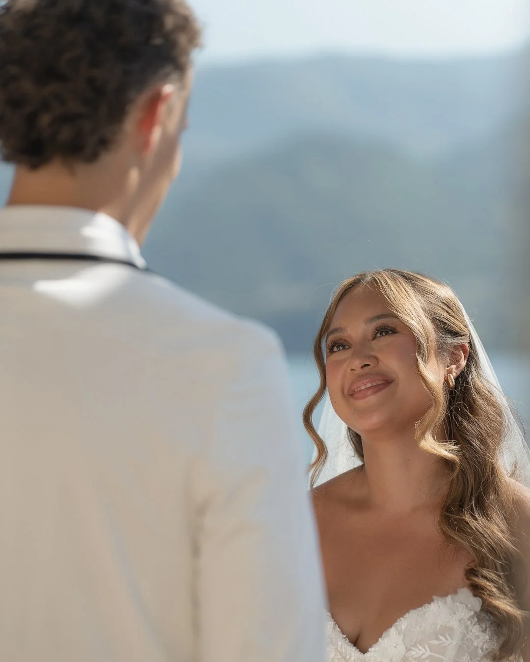 Una coppia di sposi si guarda con affetto durante il loro matrimonio, con lo sfondo di un paesaggio naturale e un lago.