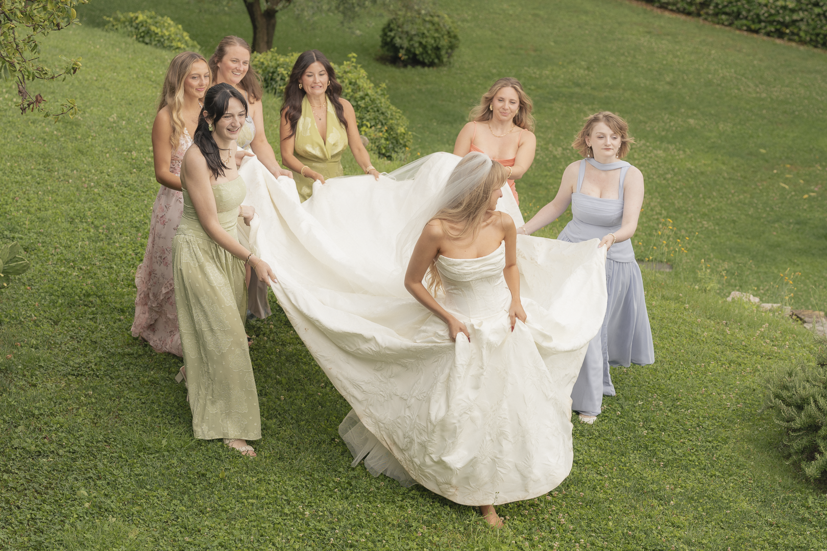 Donne che aiutano la sposa a portare il suo abito in un giardino.