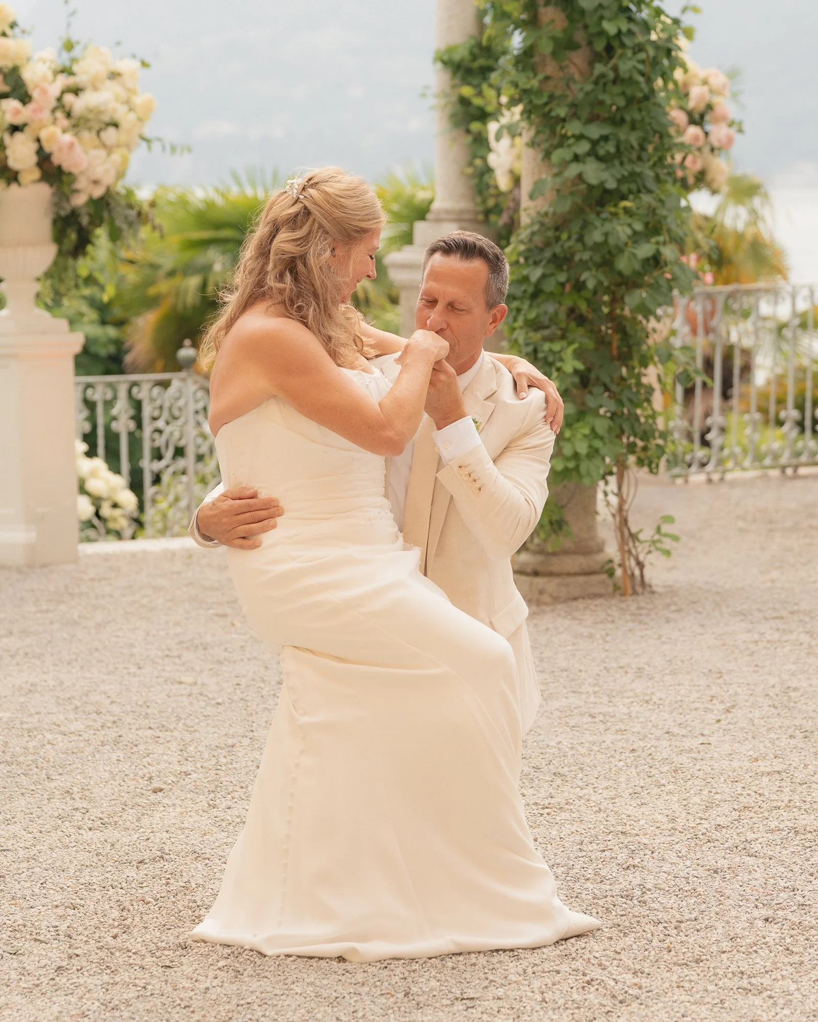 Una coppia di sposi si abbraccia e si bacia in un matrimonio all'aperto, circondati da fiori e piante verdi.