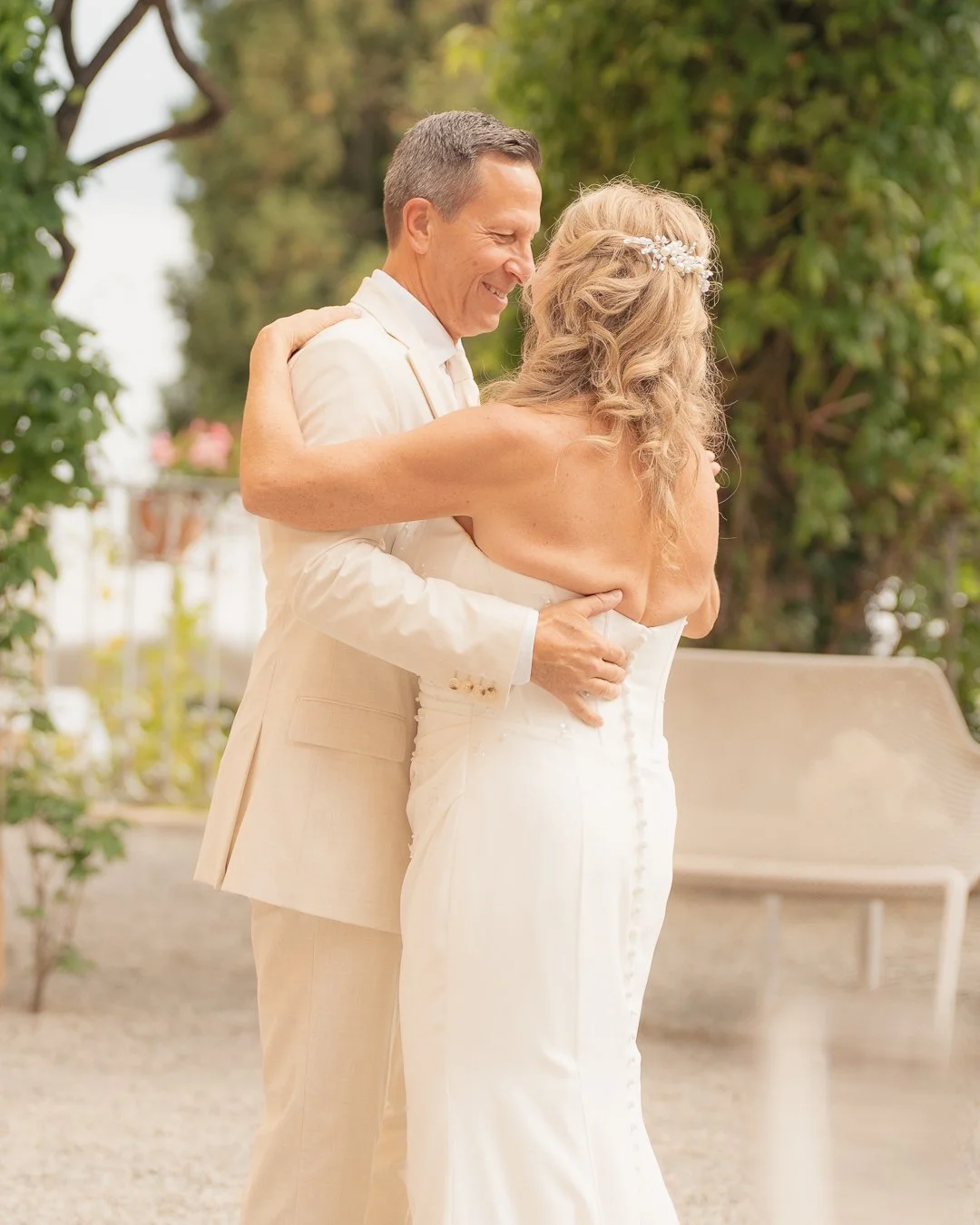 Un uomo e una donna si abbracciano in un giardino, probabilmente durante un matrimonio, entrambi sorridenti e felici.