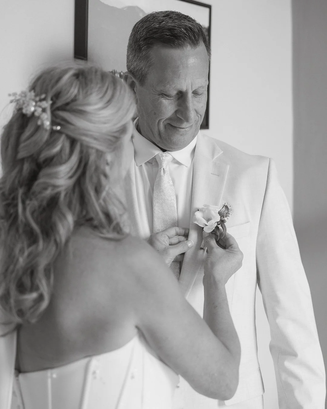 Una donna sta attaccando una boutonnière sul vestito di un uomo, presumibilmente in occasione di un matrimonio.