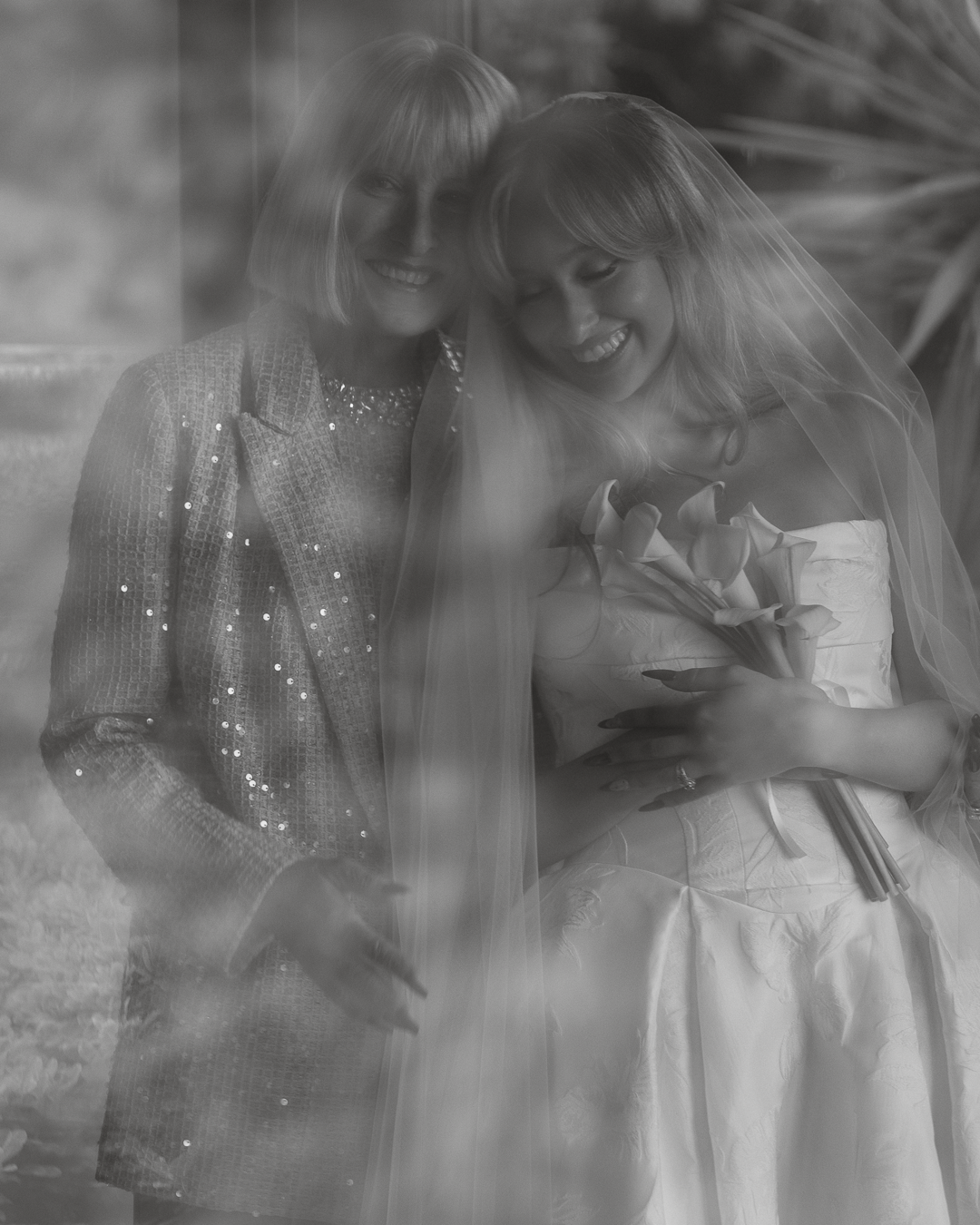 Due donne sorridenti in un abito da sposa, una con bouquet di fiori, in un'immagine in bianco e nero con effetto sfocato