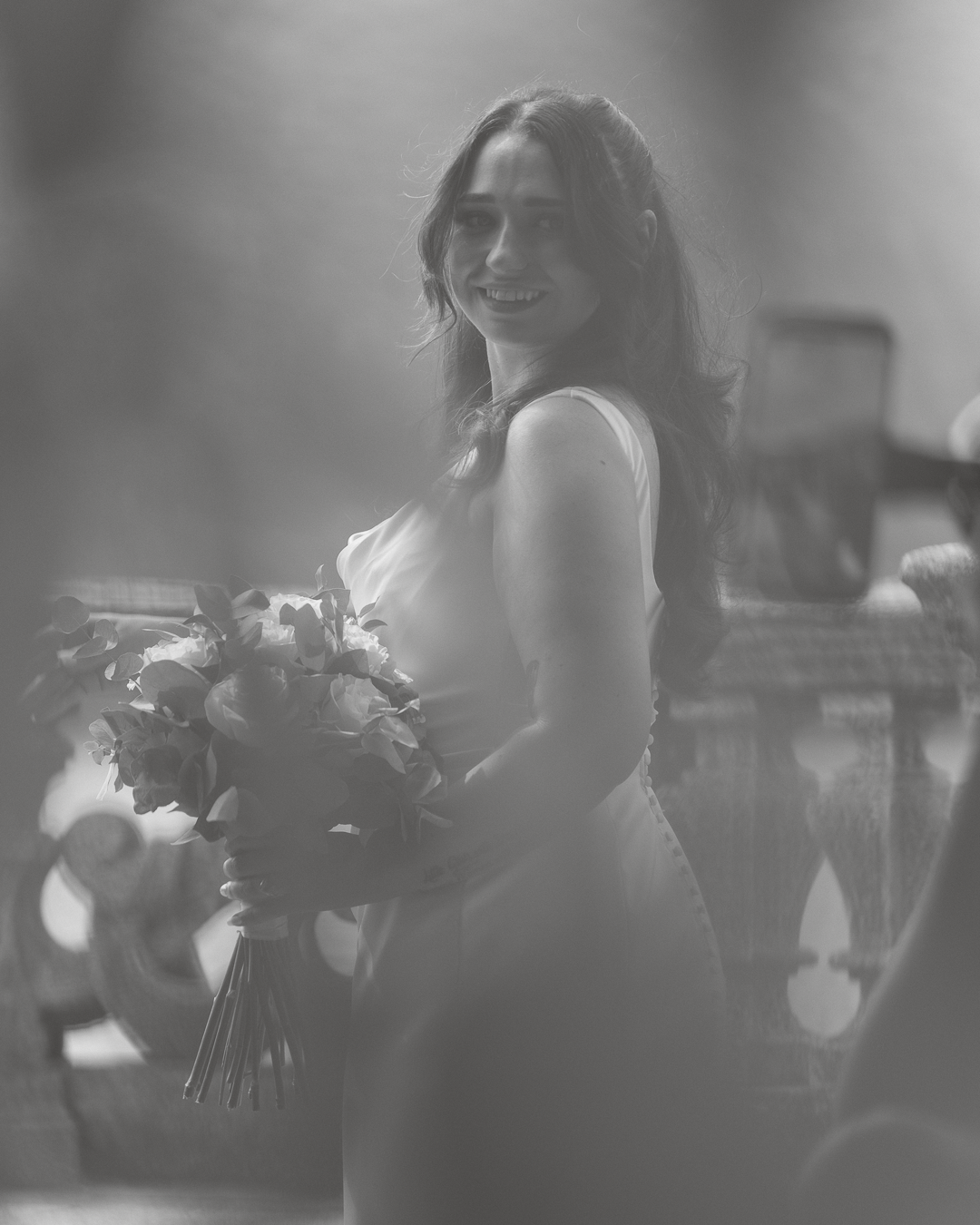 Una donna sorridente con capelli lunghi che tiene un bouquet di fiori, in un ambiente interno con decorazioni.