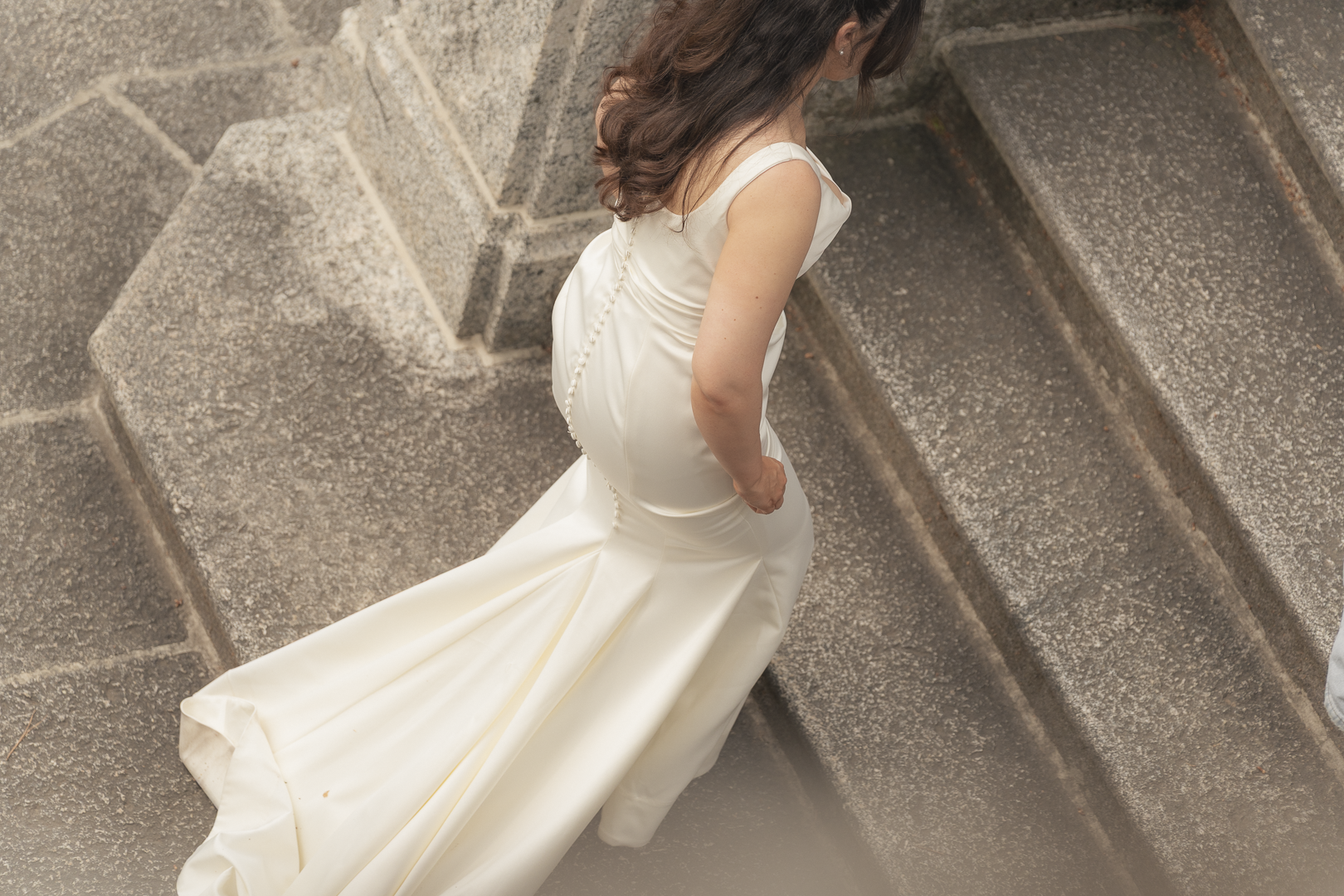 Donna in abito bianco da sposa che scende le scale in pietra.