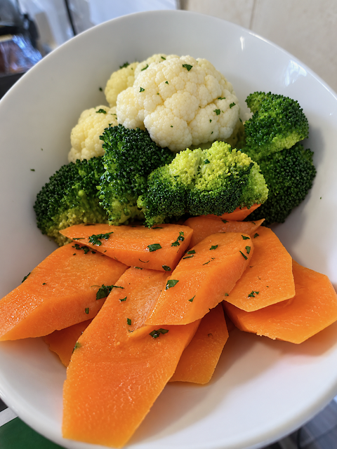 Steamed cauliflower and broccoli with sliced carrots, garnished with parsley, served on a white plate