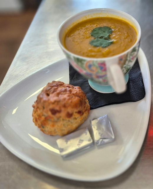 Cup of creamy soup garnished with cilantro, served with a savory biscuit and wrapped butter on a white plate