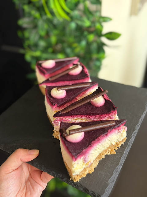Row of berry mousse cake slices topped with pink dollops and chocolate curls on a black slate board