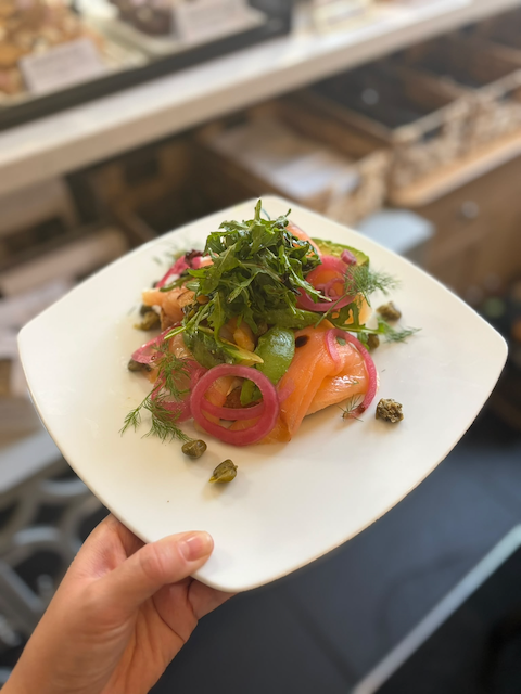 Plated smoked salmon with pickled onions, greens, herbs, and capers on a white square plate