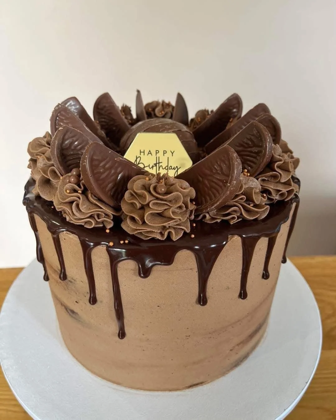 Chocolate birthday cake with chocolate drip, topped with chocolate frosting, Oreo cookies, and a white chocolate 'Happy Birthday' message.
