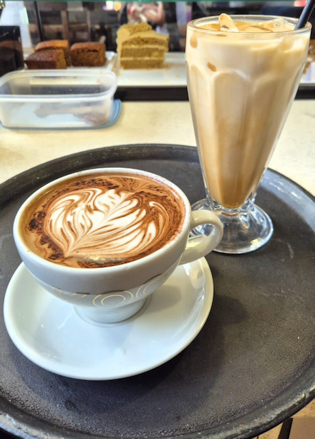 Cappuccino with latte art and an iced latte on a serving tray at a café