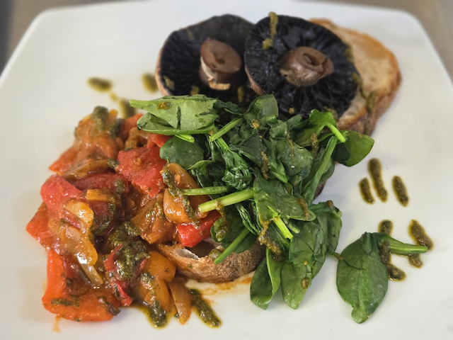 Gourmet plate with roasted portobello mushrooms, sautéed spinach, roasted vegetables, toast, and herb sauce