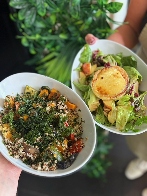 Two bowls of healthy food: a quinoa and roasted vegetable bowl with kale, and a mixed green salad topped with baked goat cheese.