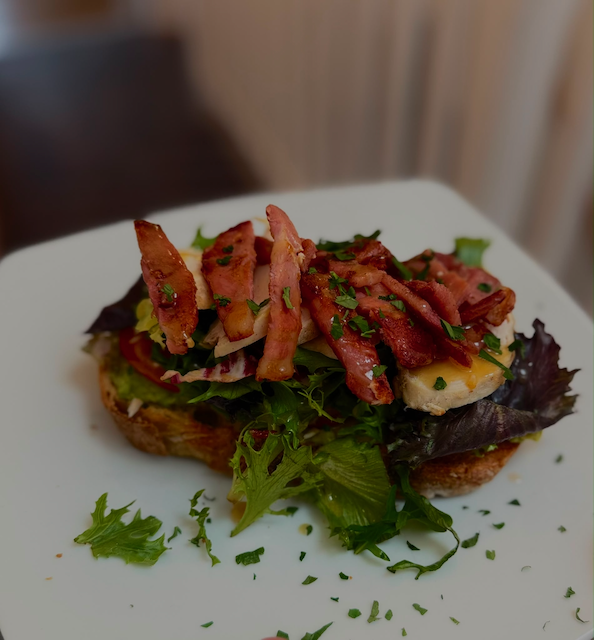 Open-faced bacon and egg sandwich with mixed greens and herbs on toasted bread