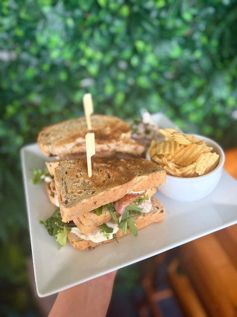 Gourmet club sandwich with greens and tomato, served with ridged potato chips on a white plate