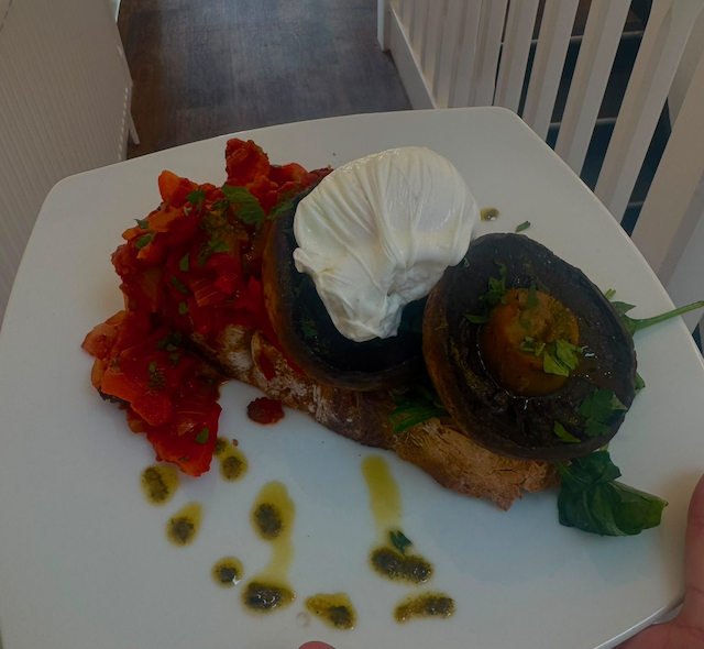 Avocado toast with poached egg, roasted tomatoes, herbs, and olive oil on a white plate