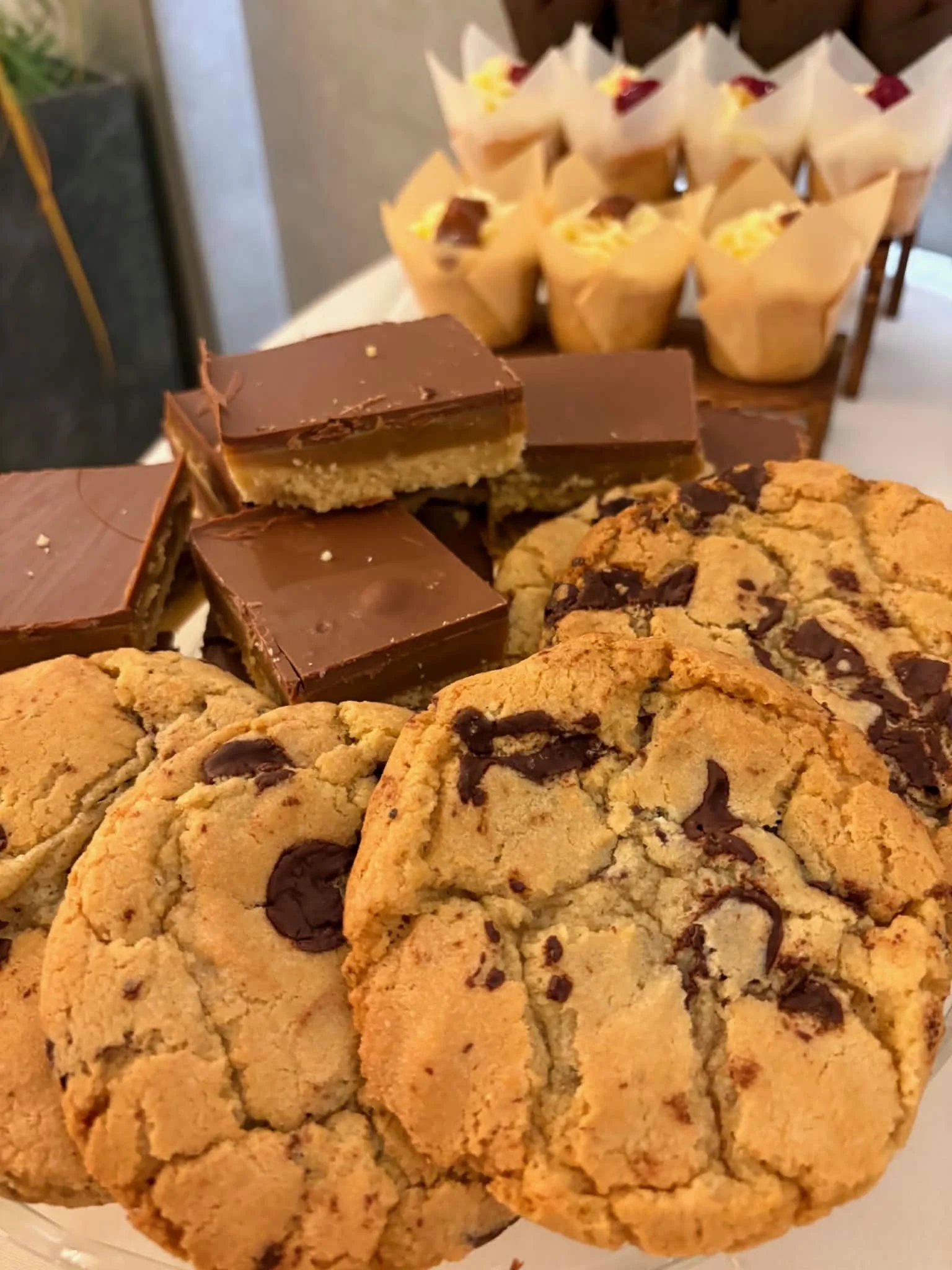 Close-up view of chocolate chip cookies in the foreground and chocolate-covered layered dessert cups in the background.