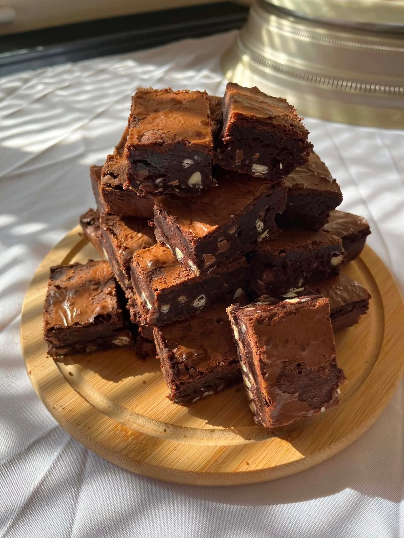 A stack of chocolate fudge brownies with nuts on a round wooden tray.