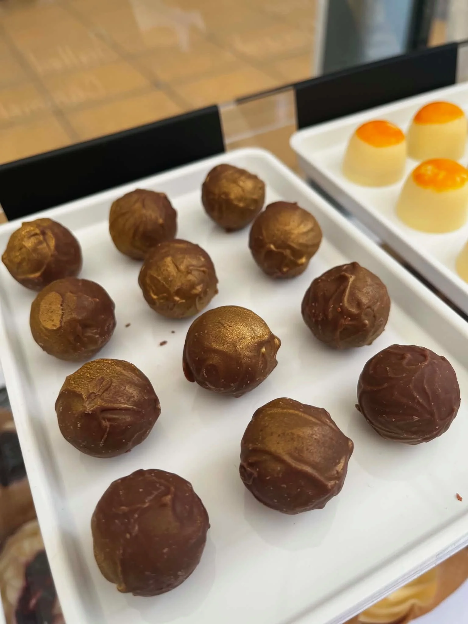 Tray of chocolate-covered hazelnuts and a tray of desserts topped with orange jelly.