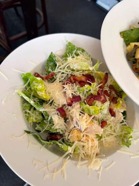 Bowl of Caesar salad with lettuce, shredded cheese, bacon bits, and croutons