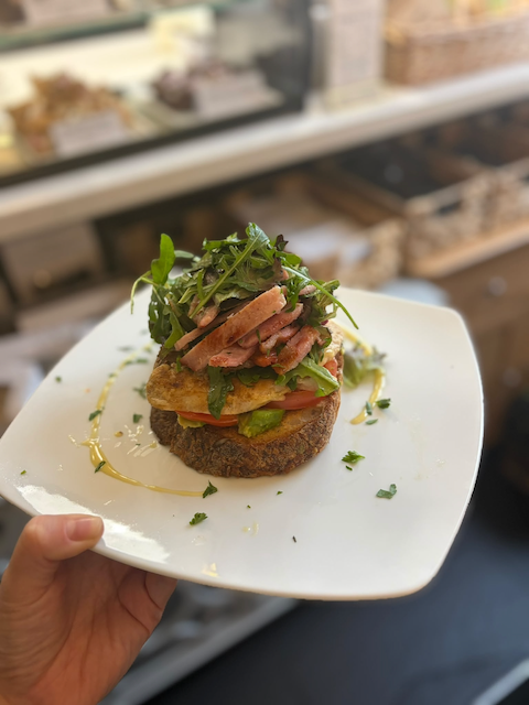 Gourmet open-faced sandwich with bacon, avocado, tomato, fried egg, and leafy greens on a white plate