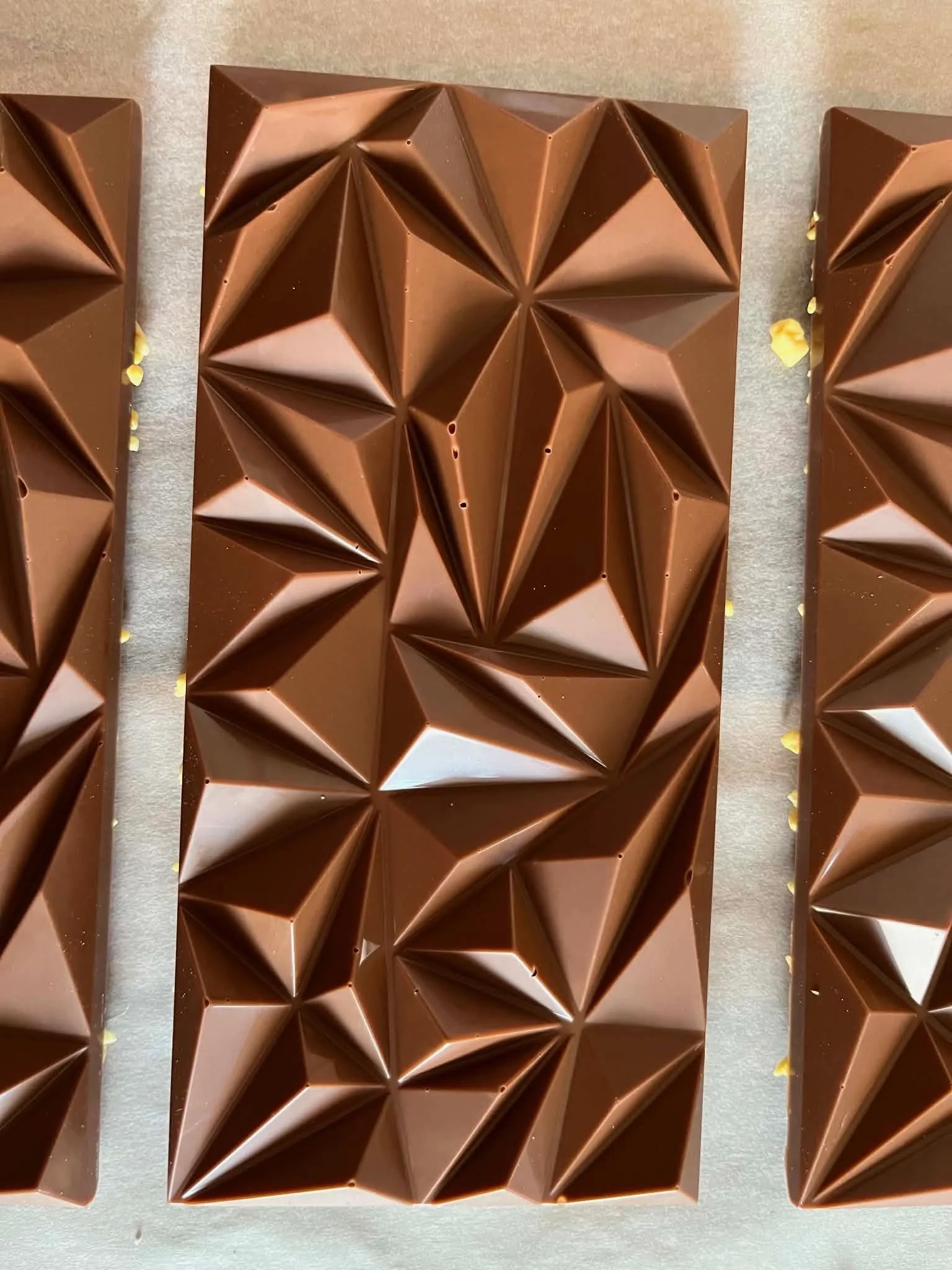 Three pieces of geometrically patterned chocolate with a shiny surface on a flat surface.