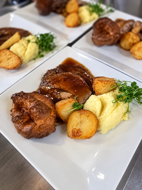 Plated roast beef with Yorkshire pudding, roasted potatoes, mashed potatoes, gravy, and greens