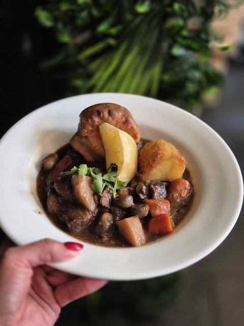 Bowl of beef stew with mushrooms, carrots, potatoes, herbs, and roasted potatoes
