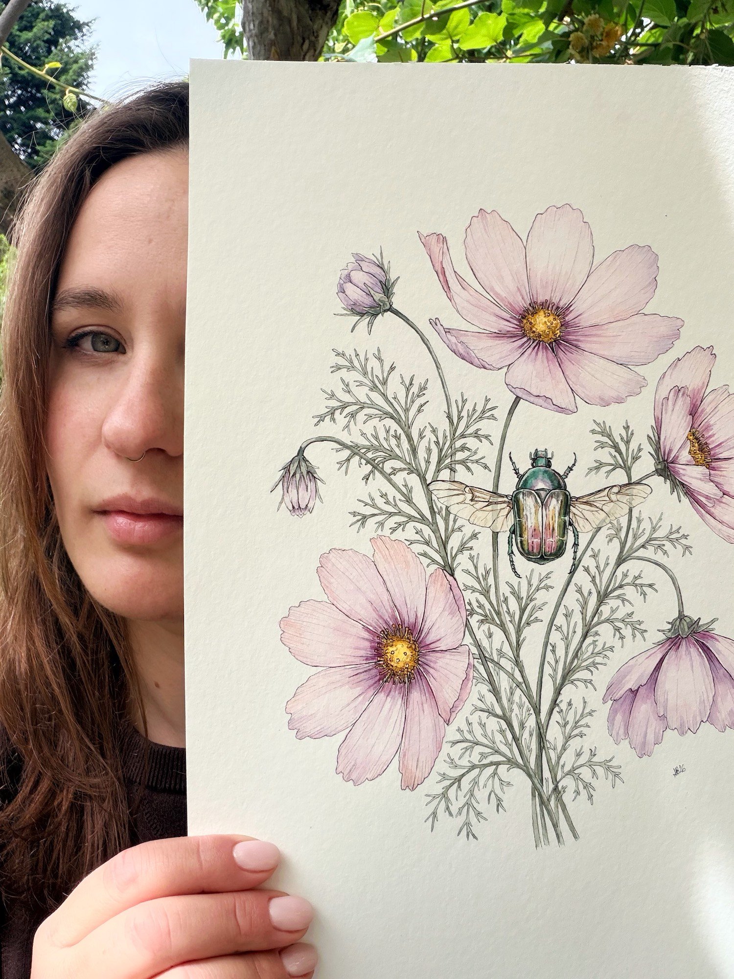 Botanical artist Alice Botanica holding an original watercolor painting of cosmos flowers and a jewel beetle.