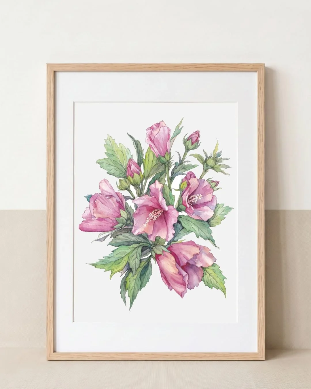 Framed botanical watercolour of pink Hibiscus syriacus (Rose of Sharon) flowers, buds and green leaves, displayed in a natural oak frame with a white mat.