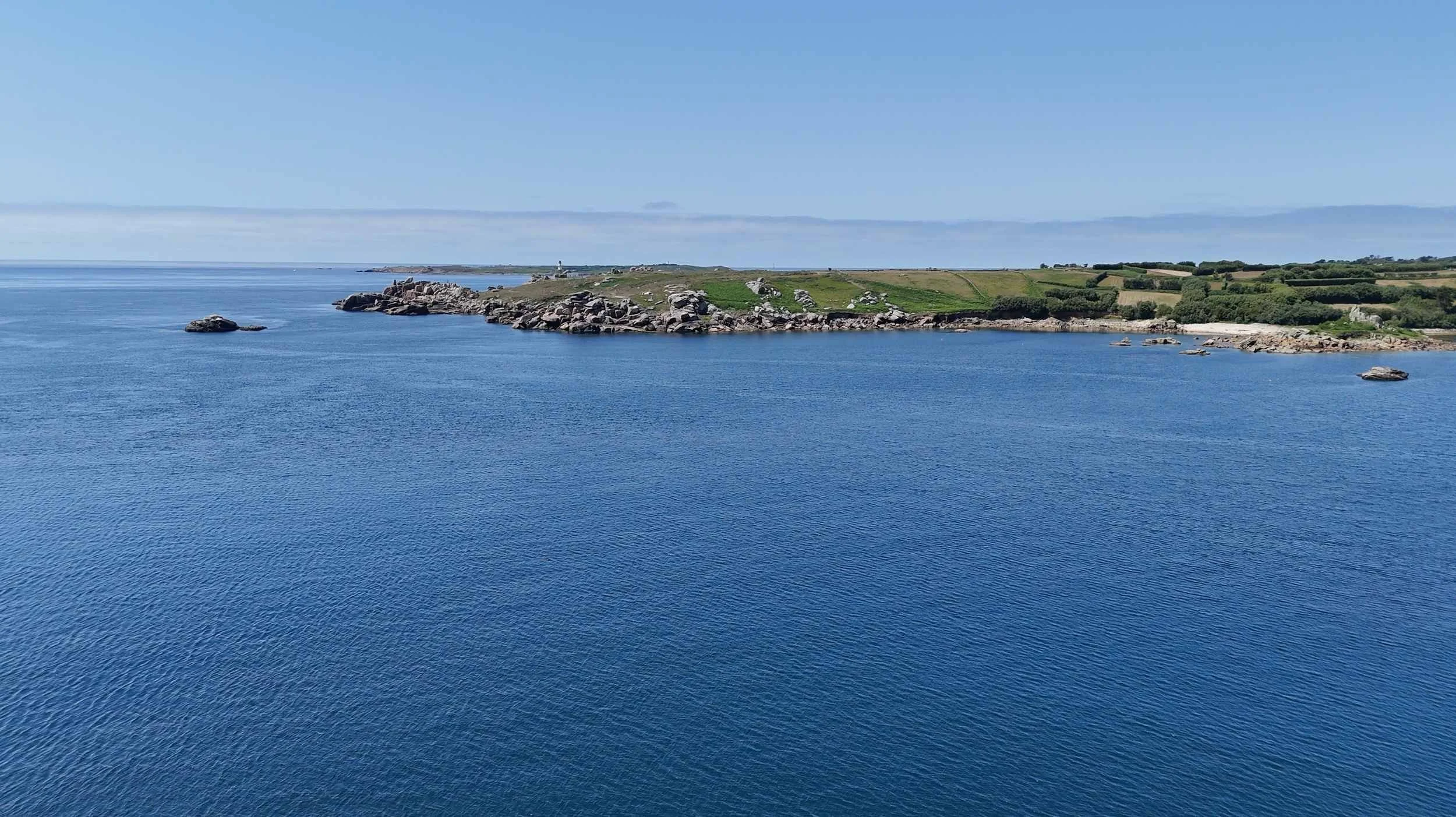 A coastal landscape with a large body of water, rocky shoreline at the edge of Peninnis headland under a clear blue sky.