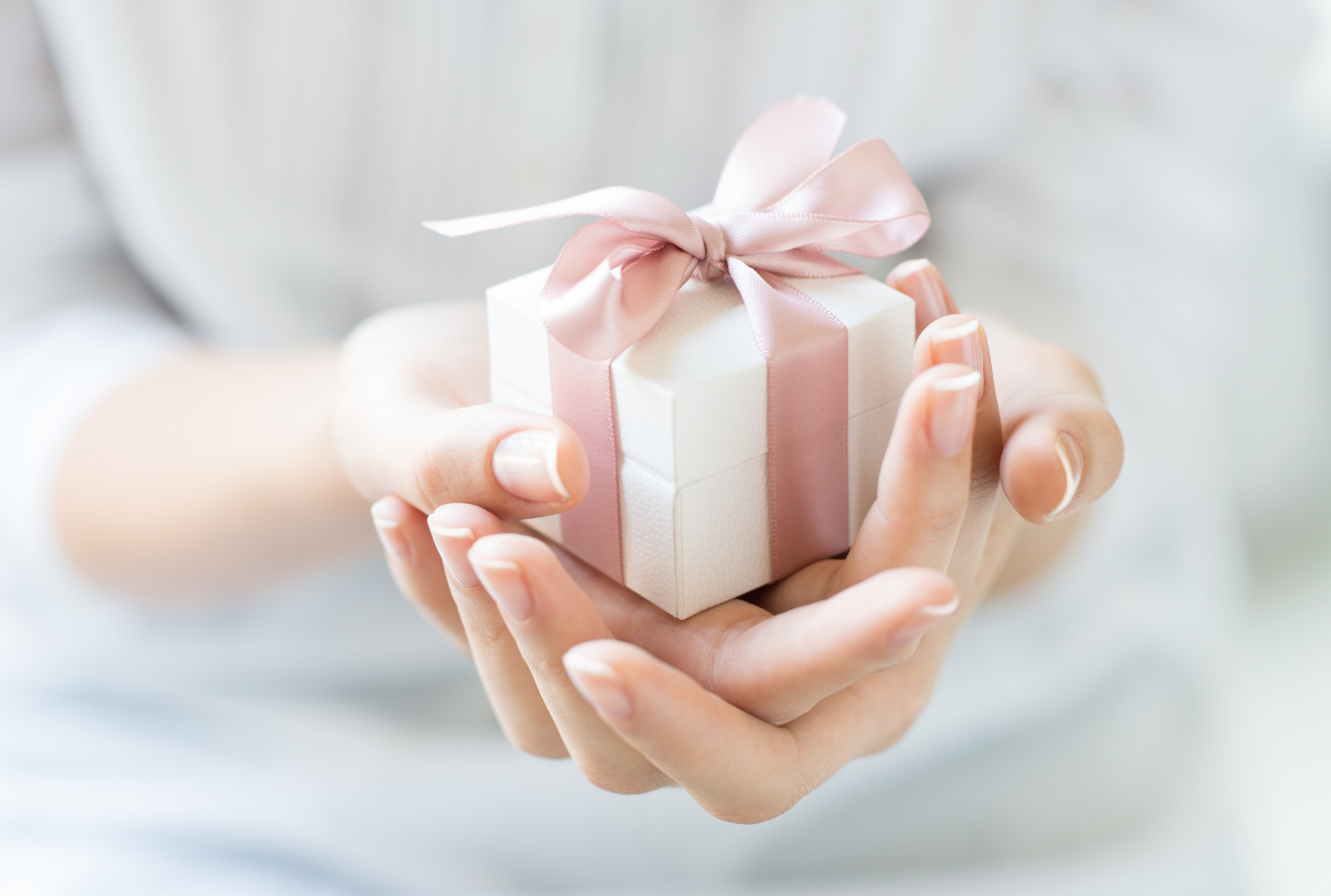 Person holding a small white gift box with pink ribbon and bow.