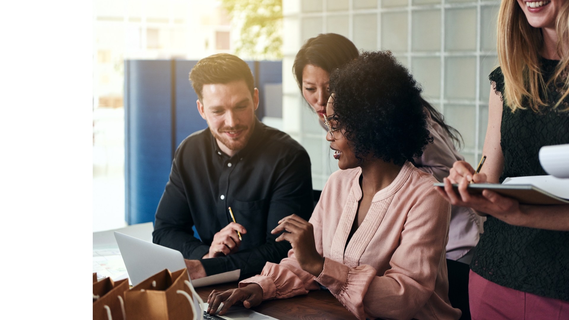 Group of five diverse coworkers working together in an office, collaborating around a table with laptops and documents.